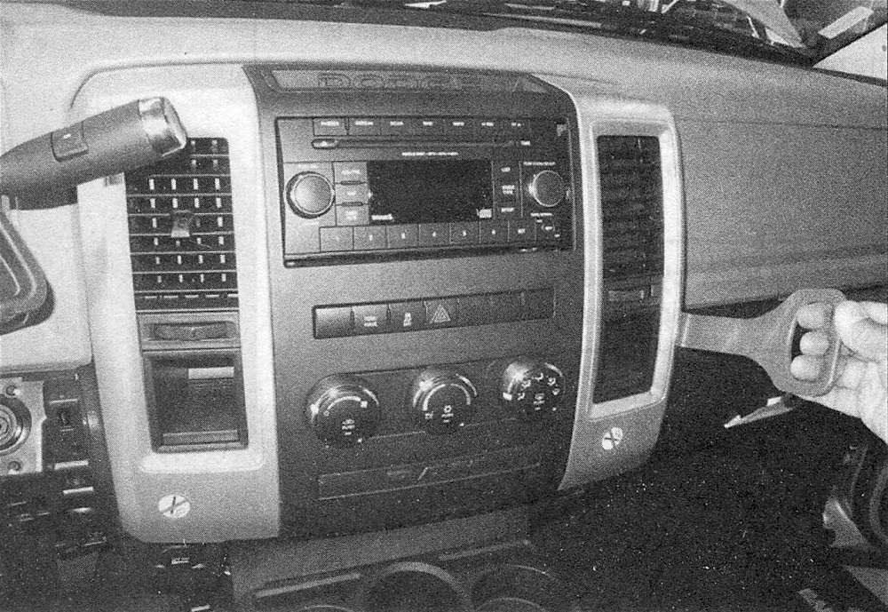 Ram Trucks Radio and speakers - After removing the two screws under the upper storage tray, use a plastic trim tool to pull the center bezel rearward